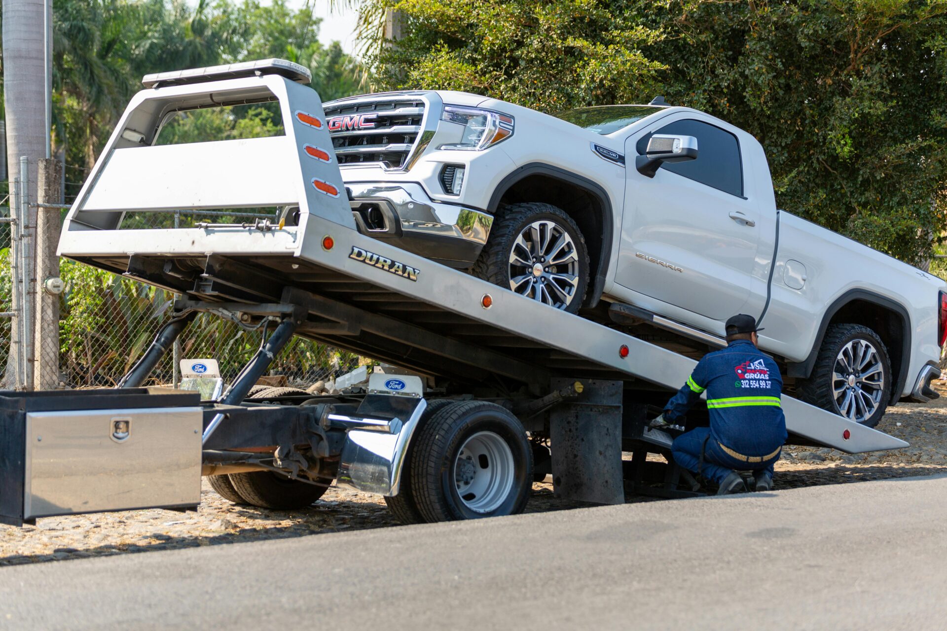 A tow truck operator loads a pickup truck onto a flatbed for roadside recovery